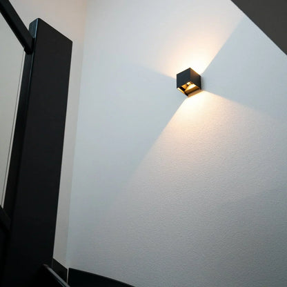Svart vägglampa på vit vägg vid en trappa, sedd underifrån med ljuskäglor 8