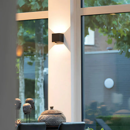Svart vägglampa på en vit pelare mellan fönster med utsikt mot trädgård 7