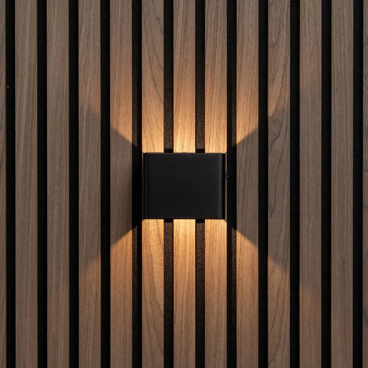Svart vägglampa rakt framifrån på träpanel, varmt ljus uppåt och nedåt 5