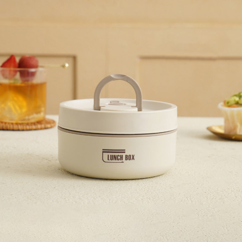 Weiße runde Lunchbox mit Griff auf Tisch, ideal für Mahlzeiten unterwegs, modernes Design.