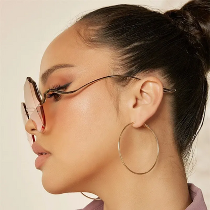 Frau mit luxuriöser Sonnenbrille, Farbverlaufsgläser, goldene Creolen, modisches Accessoire.