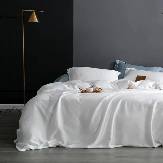 Luxuriöses weißes Seidenbettwäsche-Set auf modernem Doppelbett mit Nachttischlampe.