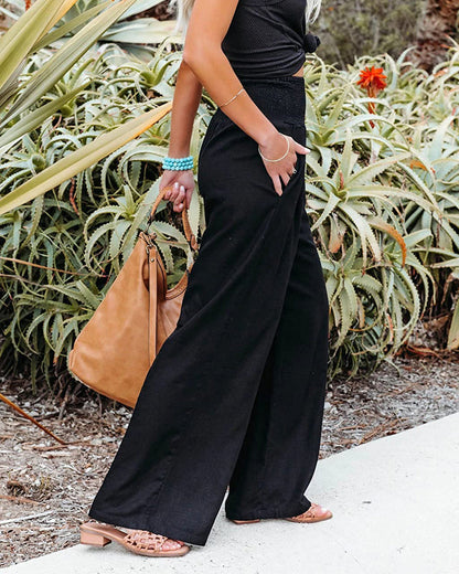Frau in schwarzer Hose, braune Ledertasche, Sommermode, lässiger Stil, Gartenhintergrund.