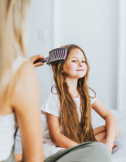 Mädchen mit langen Haaren wird mit lila Kamm gekämmt, Kind, Haarpflege, Zuhause.