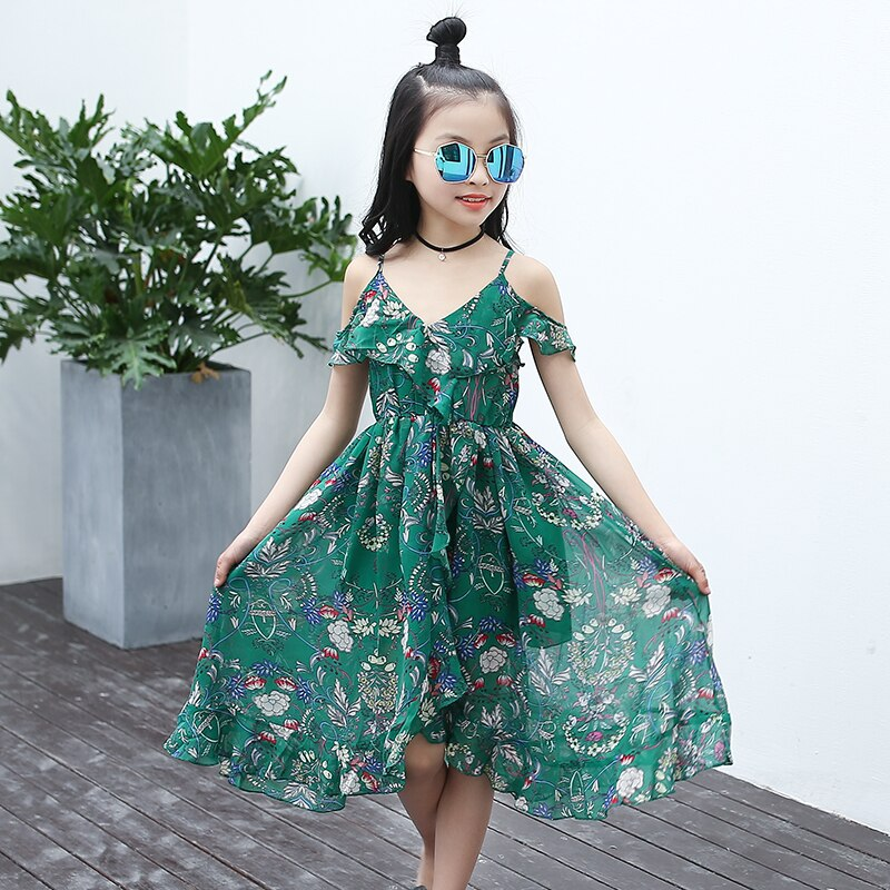 Mädchen in grünem Boho-Sommerkleid mit Blumenmuster, Sonnenbrille, draußen.