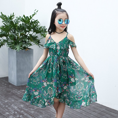 Mädchen in grünem Boho-Sommerkleid mit Blumenmuster, Sonnenbrille, draußen.