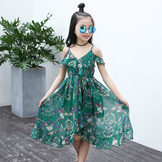 Mädchen in grünem Boho-Sommerkleid mit Blumenmuster, Sonnenbrille, draußen.