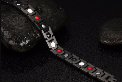 Schwarzes magnetisches Armband mit roten und weißen Elementen auf nassem Stein.