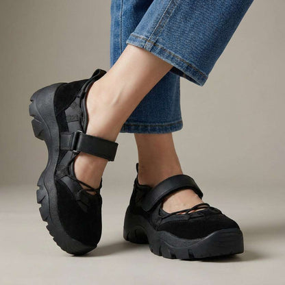 Studiobild av helsvarta skor med kardborrerem och grov sula, bärda med blå jeans. 5