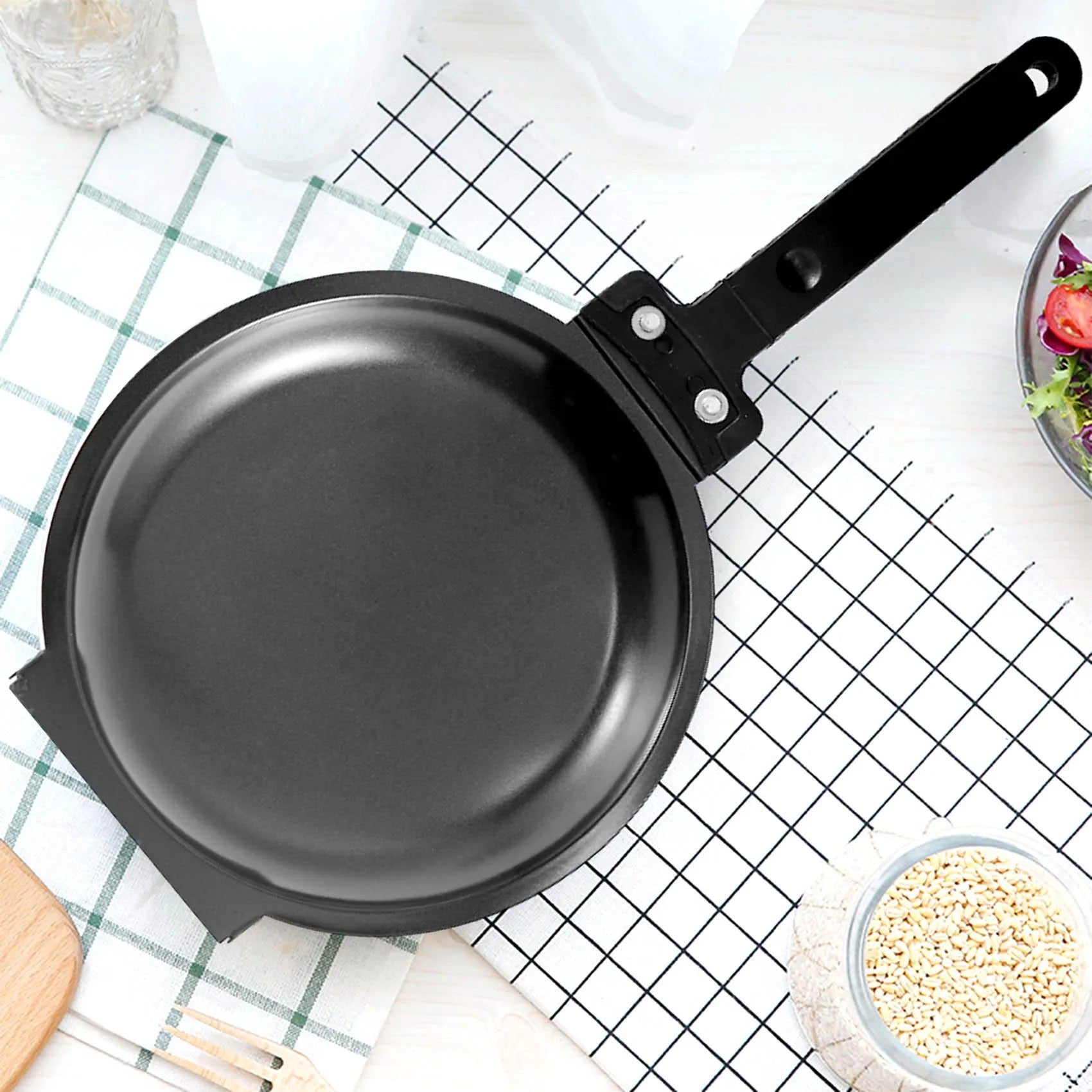 Schwarze Antihaft-Pfanne mit Griff auf kariertem Küchentuch, ideal zum Braten und Kochen.