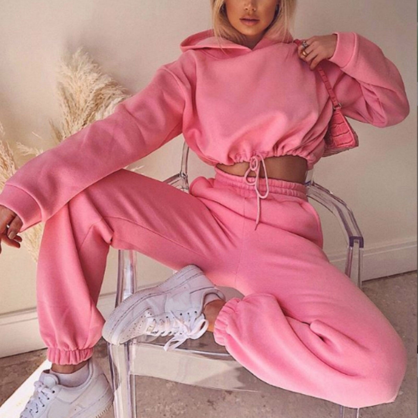 Frau in rosa Jogginganzug auf transparentem Stuhl, weiße Sneaker, modisch, bequem, Freizeitkleidung.