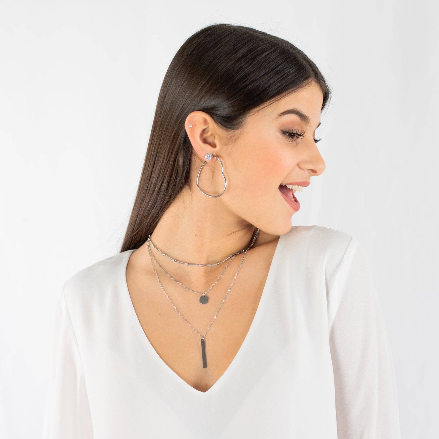 Frau mit silberner Halskette und Ohrringen, weißes Oberteil, modischer Schmuck, lächelnd.