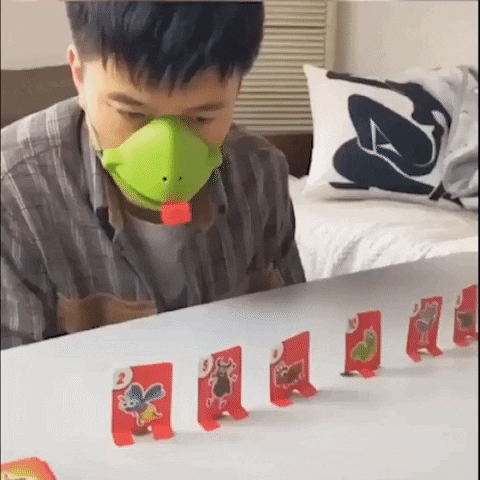 Mann mit grüner Schweinemaske spielt mit roten Karten auf einem Tisch.