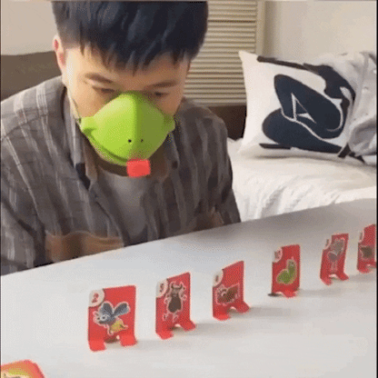 Mann mit grüner Schweinemaske spielt mit roten Karten auf einem Tisch.