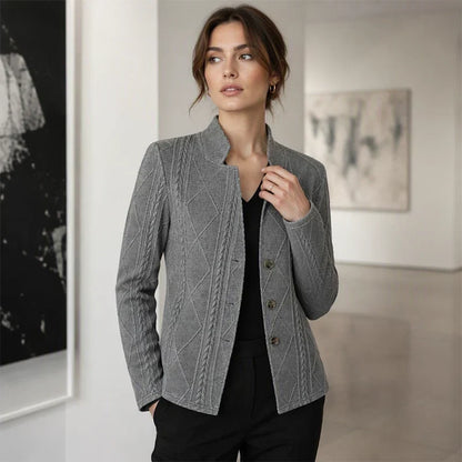 Grå strukturerad blazer bärd över svart topp av en kvinna som står i ett ljust galleri med handen i fickan. 11