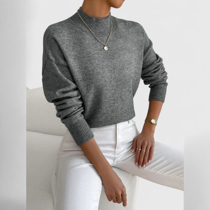 Modell i grå melerad polotröja med ribbad krage och muddar, vita jeans och ett enkelt halsband med hänge. 12