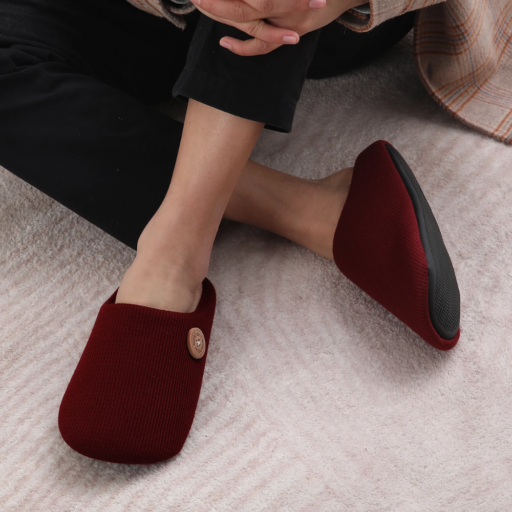 Rote Memory-Foam-Hausschuhe, bequem, rutschfest, mit Knopfdetail, auf Teppich.