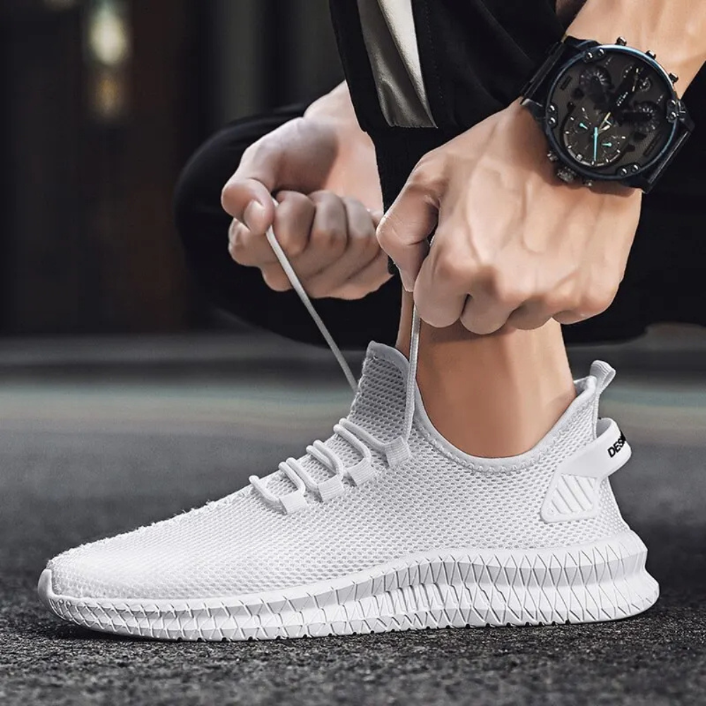 Weiße Herren-Sneaker, atmungsaktiv, sportlich, mit Schnürsenkeln, auf Asphalt getragen.