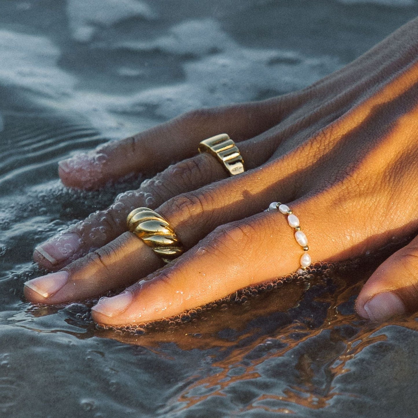 Hand mit goldenen Ringen und Perlenring im Wasser, Schmuck, Modeaccessoire, elegantes Design.