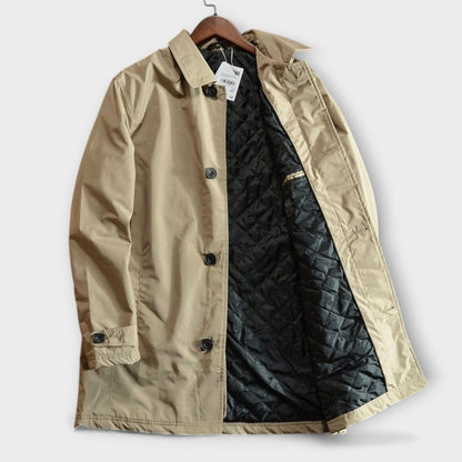 Beige kappa på galge, framifrån med öppen front som visar det svarta quiltade fodret och svarta knappar. 7