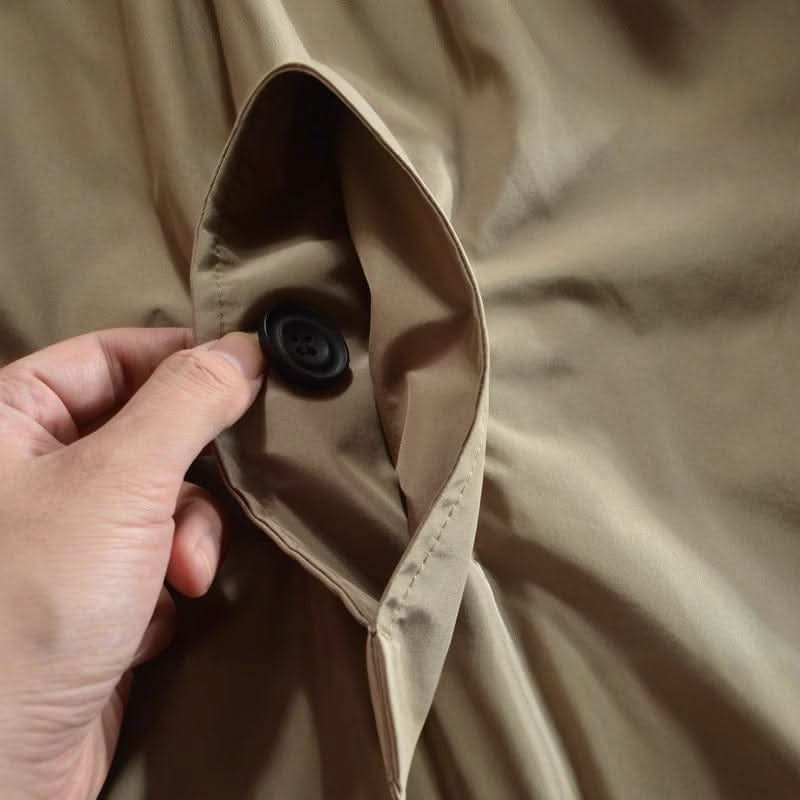 Närbild på en hand som håller upp en ficka i beige tyg med en svart knapp inuti. 8