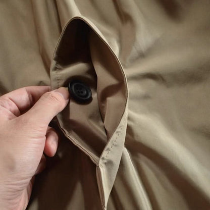 Närbild på en hand som håller upp en ficka i beige tyg med en svart knapp inuti. 8