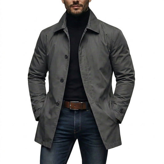 Man bär den grå kappan öppen över svart polotröja och jeans, med händerna i fickorna, sedd framifrån. 1