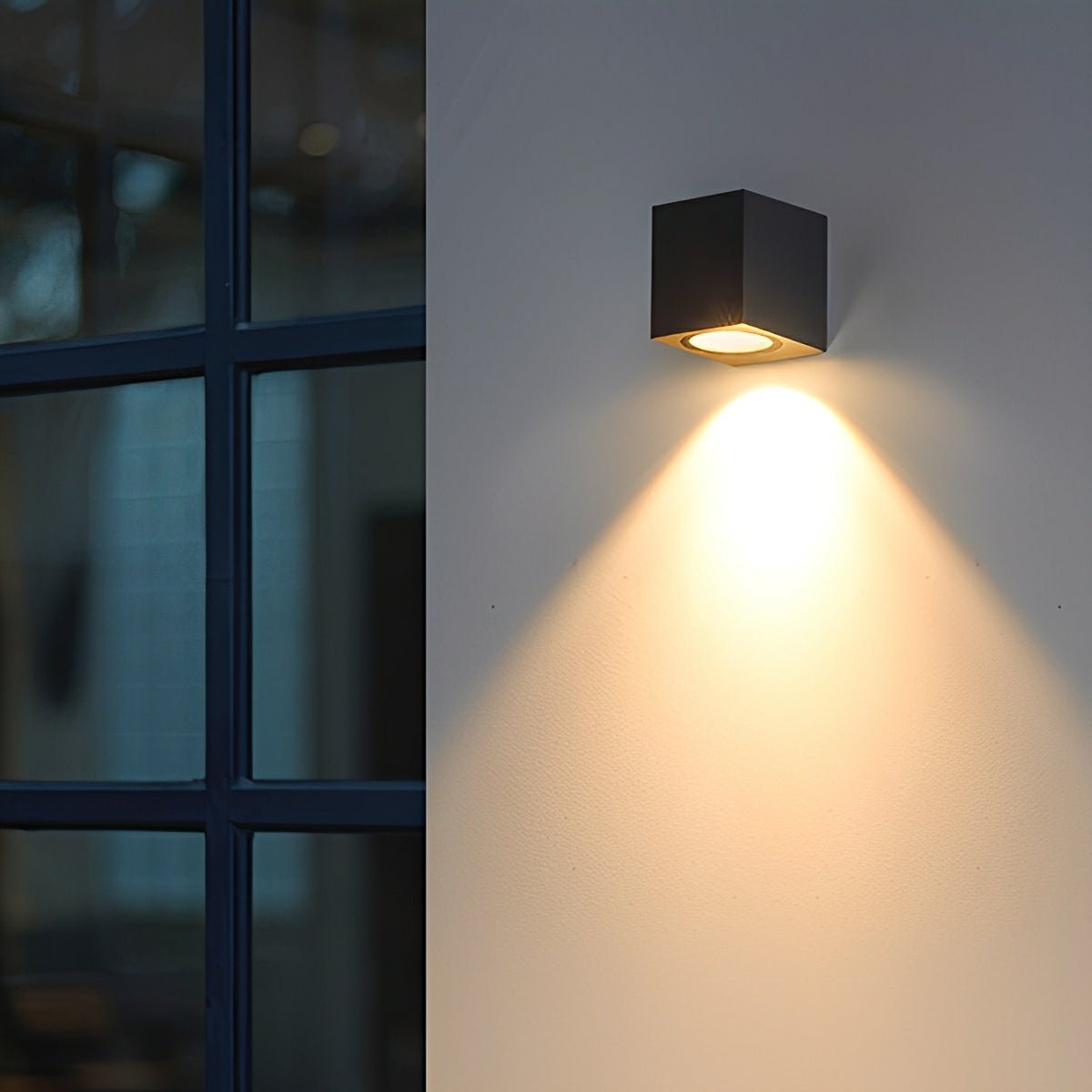 Svart kubformad vägglampa med nedåtriktat ljus på en vägg bredvid ett spröjsat fönster 11