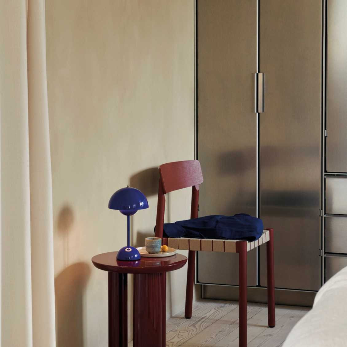 Moderner Innenraum mit blauer Tischlampe, rotem Stuhl und Metallkleiderschrank.