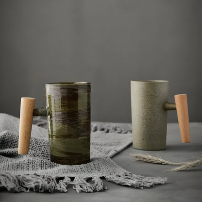 Två muggar med trähandtag, en grönbrun och en beige, på grå textil med vetestrå 1