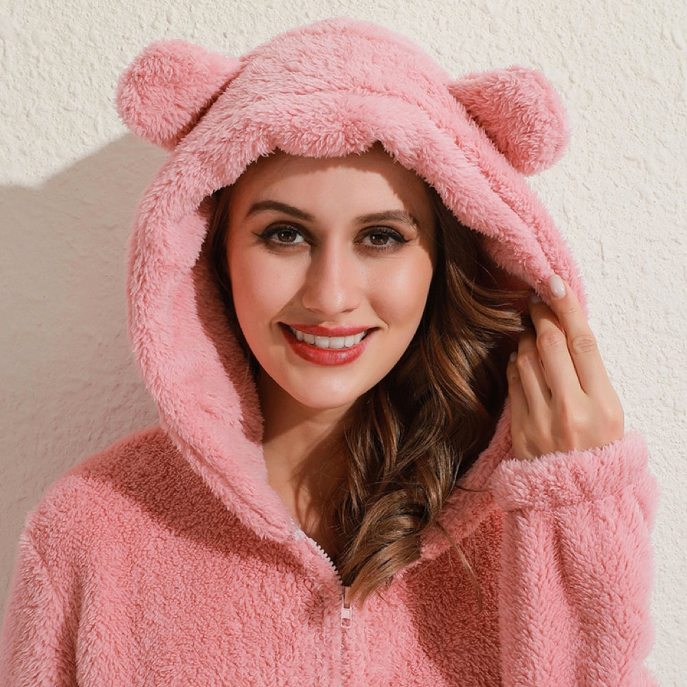 Frau in rosa Plüsch-Overall mit Kapuze und Bärenohren, gemütliche Damenbekleidung.