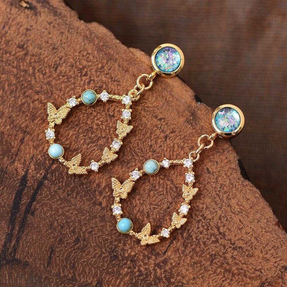 Goldene Ohrringe mit Opal, Zirkonia und Schmetterlingsdesign auf Holzoberfläche.