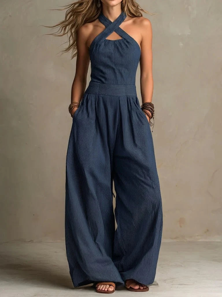 Kvinna i marinblå, finrandig jumpsuit med korsade halsband, hög midja och vida ben, händerna i fickorna, sedd framifrån. 3
