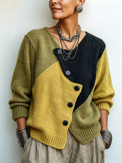 Närbild framifrån av stickad tröja i olivgrönt, senapsgult och svart med diagonala färgfält och snedställd knapplist, bärd med kedjehalsband. 1