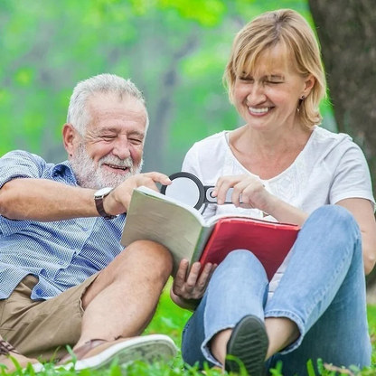 Älteres Paar im Park, lächelnd, mit Buch, Sommer, Freizeit, Natur, Entspannung, grüne Wiese.