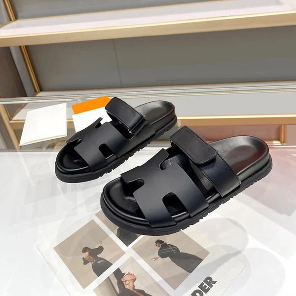 Schwarze Leder-Sandalen mit Klettverschluss auf weißem Tisch, modisch und bequem.