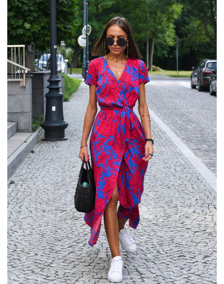 Frau in rotem und blauem Sommerkleid mit Sneakers auf gepflasterter Straße.