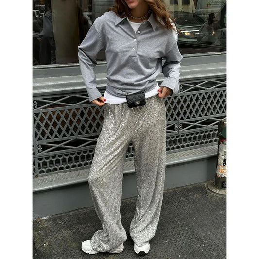 Frau in silberner Paillettenhose, grauem Hemd, weiße Sneaker, modisch, urbaner Stil.