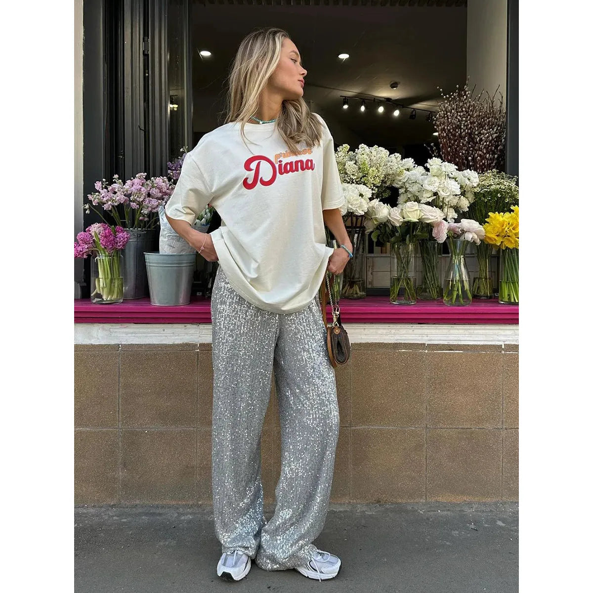 Frau in silberner Paillettenhose und weißem T-Shirt vor Blumenladen.