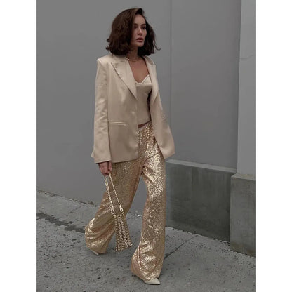 Frau in goldener Paillettenhose und cremefarbenem Blazer, modisch, elegant, urbaner Stil.