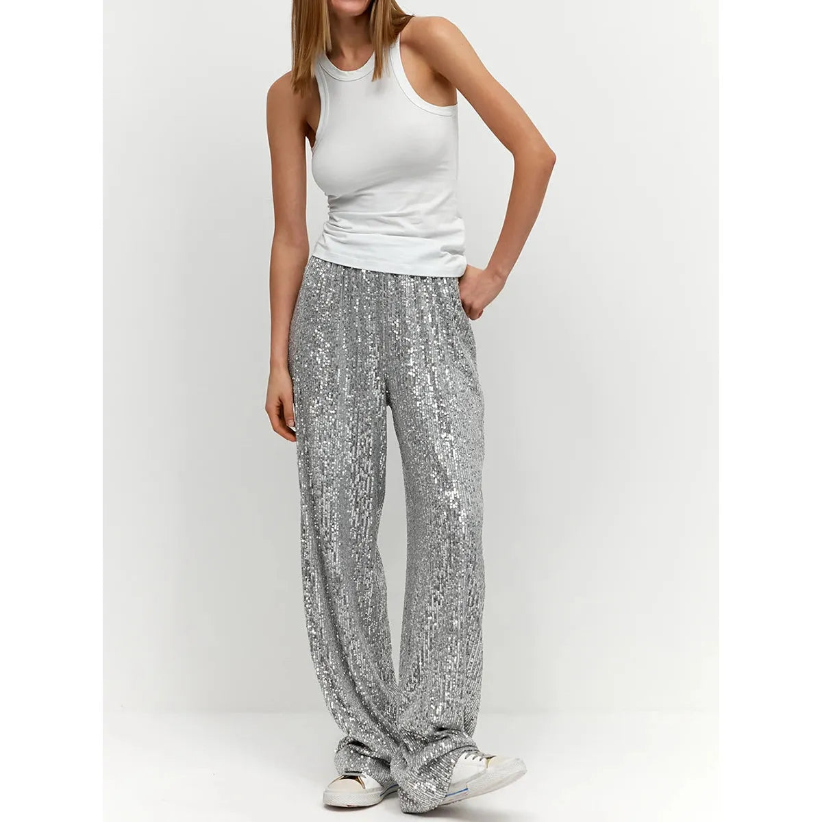 Frau trägt silberne Paillettenhose, weißes Tanktop, lässiger Look, modisch, elegant.