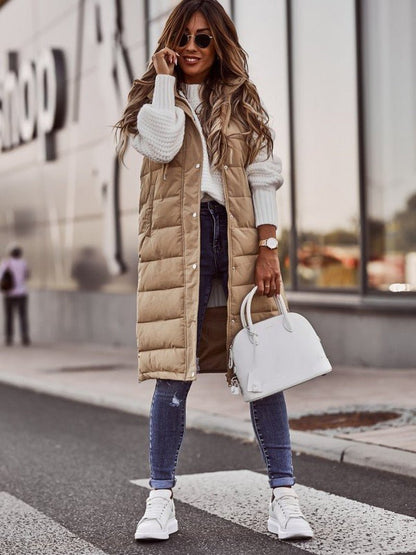 Frau in beige, knielanger Steppweste, weiße Sneakers, Jeans, weiße Handtasche, Straße.