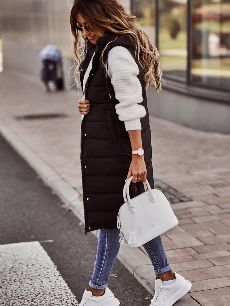Frau in schwarzer, knielanger Steppweste, weiße Tasche, Jeans, Sneakers, Herbstmode.