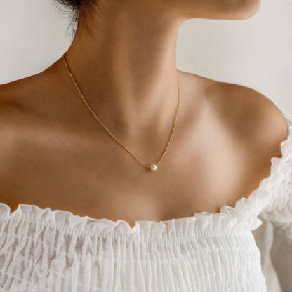Frau trägt goldene Halskette mit Perle, eleganter Schmuck, minimalistisches Design.