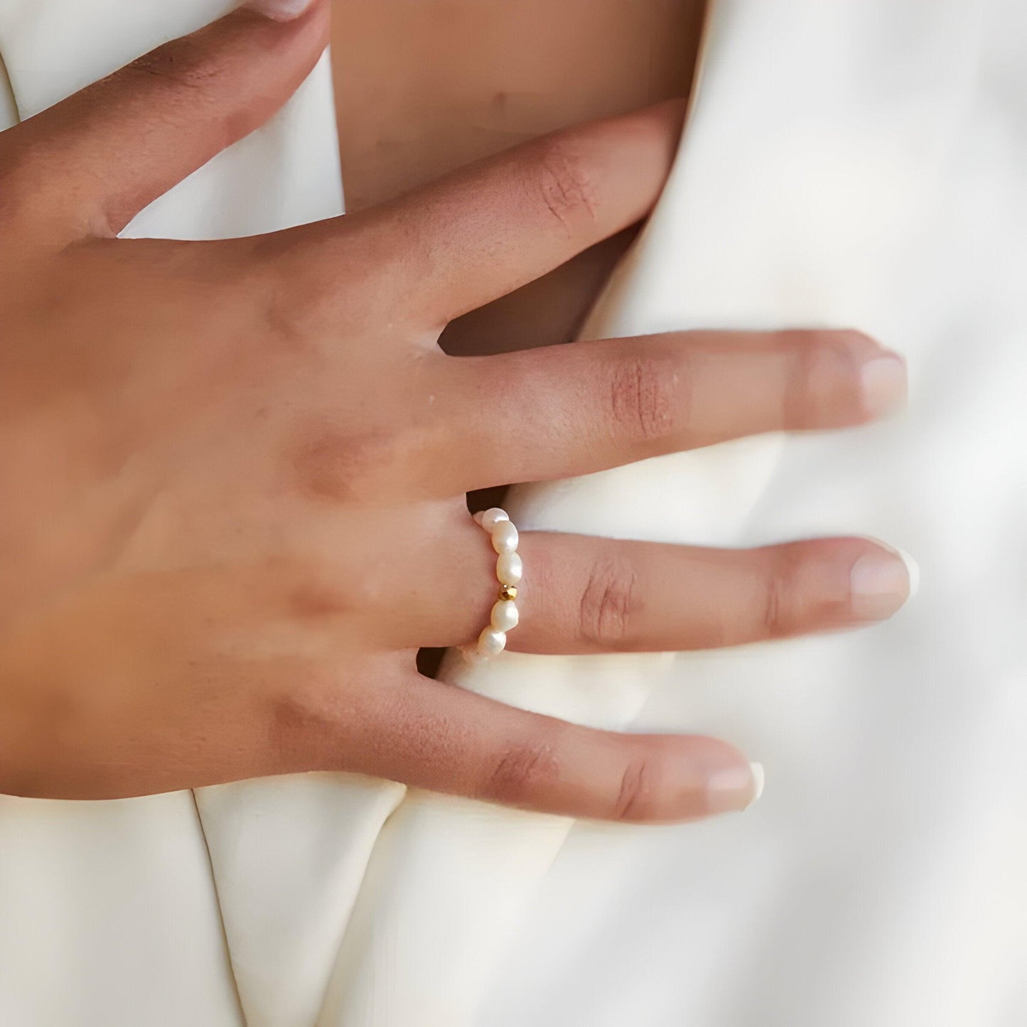 Hand mit Perlenring, Damenmode, eleganter Schmuck, weißes Outfit, stilvolles Accessoire