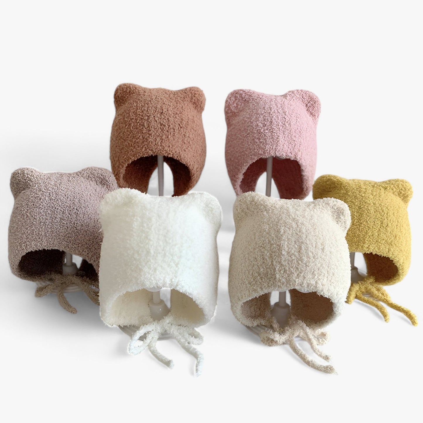 Sechs Baby-Mützen mit Bärenohren, flauschig, in verschiedenen Farben, auf weißem Hintergrund.