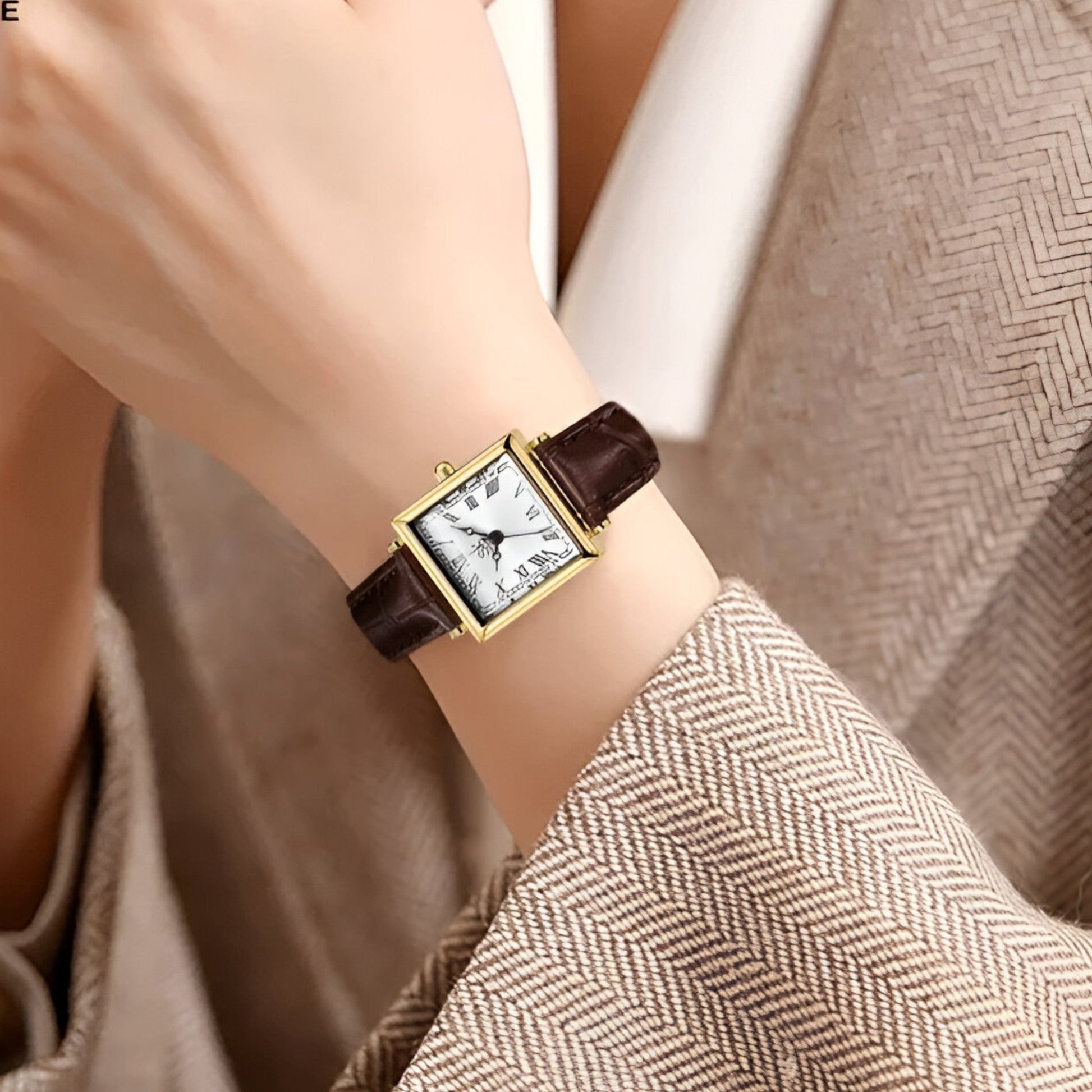 Goldene rechteckige Armbanduhr mit braunem Lederarmband auf Handgelenk, elegantes Design.