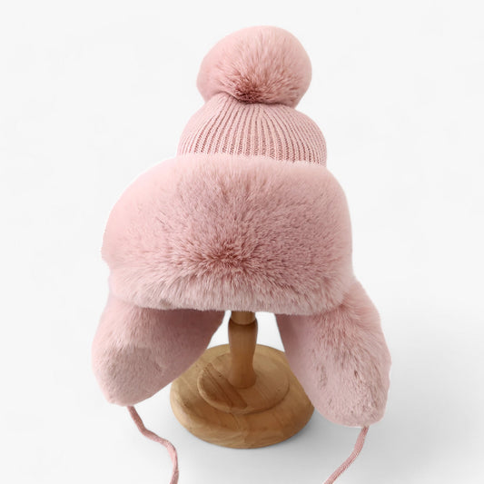 Rosa Wintermütze mit Kunstfell, Bommel und Ohrenklappen, warm, modisch, Damenaccessoire.