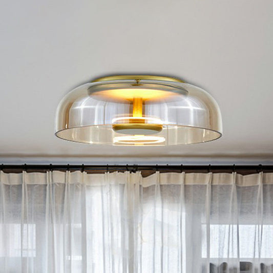 Taklampa med bärnstensfärgad glasskärm och mässingsfärgade detaljer, tänd, framför vita gardiner 2