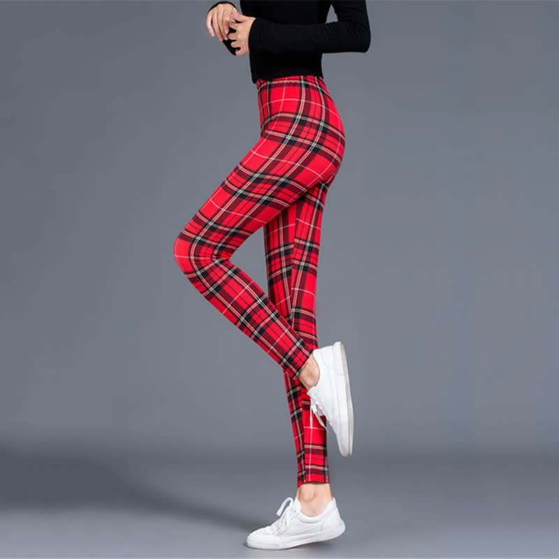 Frau in roten karierten Leggings und weißen Sneakers, seitliche Ansicht, grauer Hintergrund.